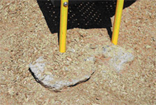 Children's play equipment support base with exposed concrete footing due to low wood chip protective surface covering